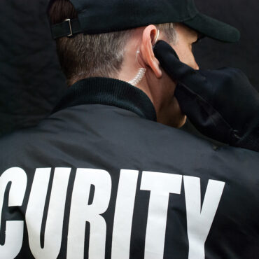 Close-up of a security guard listening to his earpiece. Back of jacket showing.